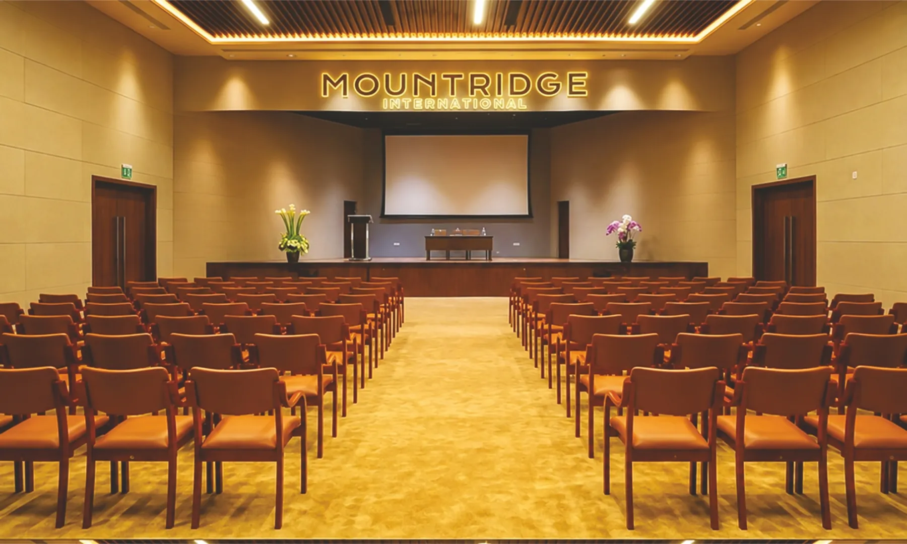 Sabha mini hall with rows of chairs facing a stage and screen beneath the Mountridge International sign