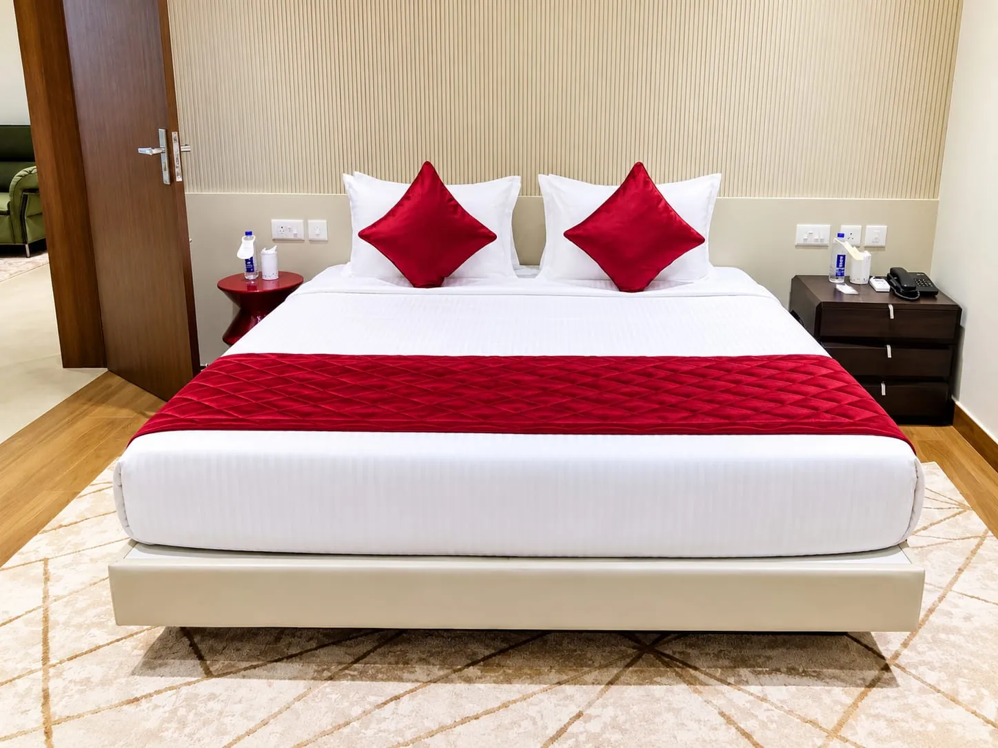 Executive Suite bedroom with a queen bed dressed in white and crimson, between walnut bedside tables
